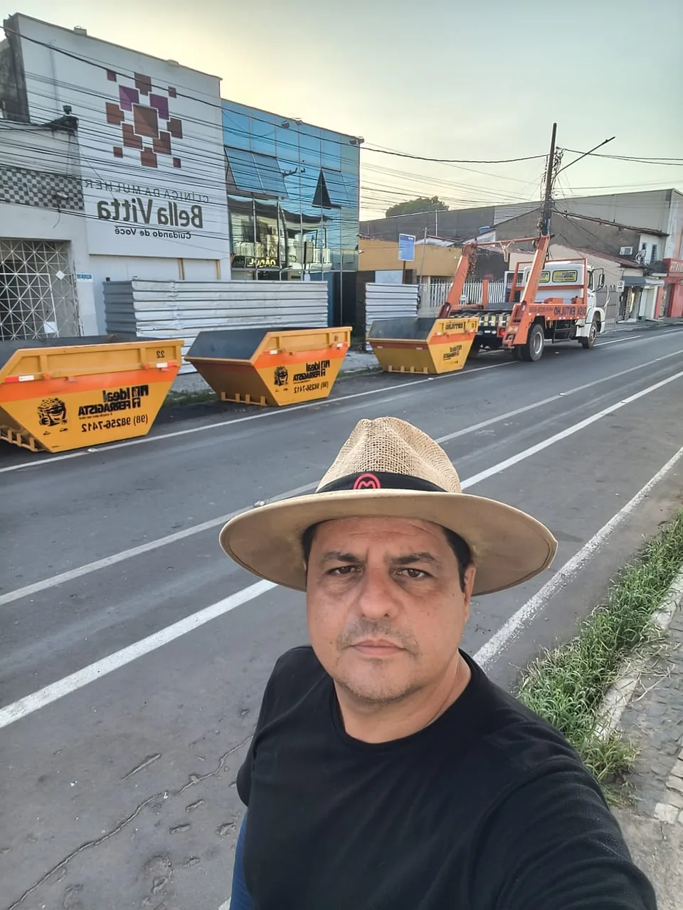 Responsável pela Ideal Ferragista de chapéu na rua, com as caçambas laranja ao fundo